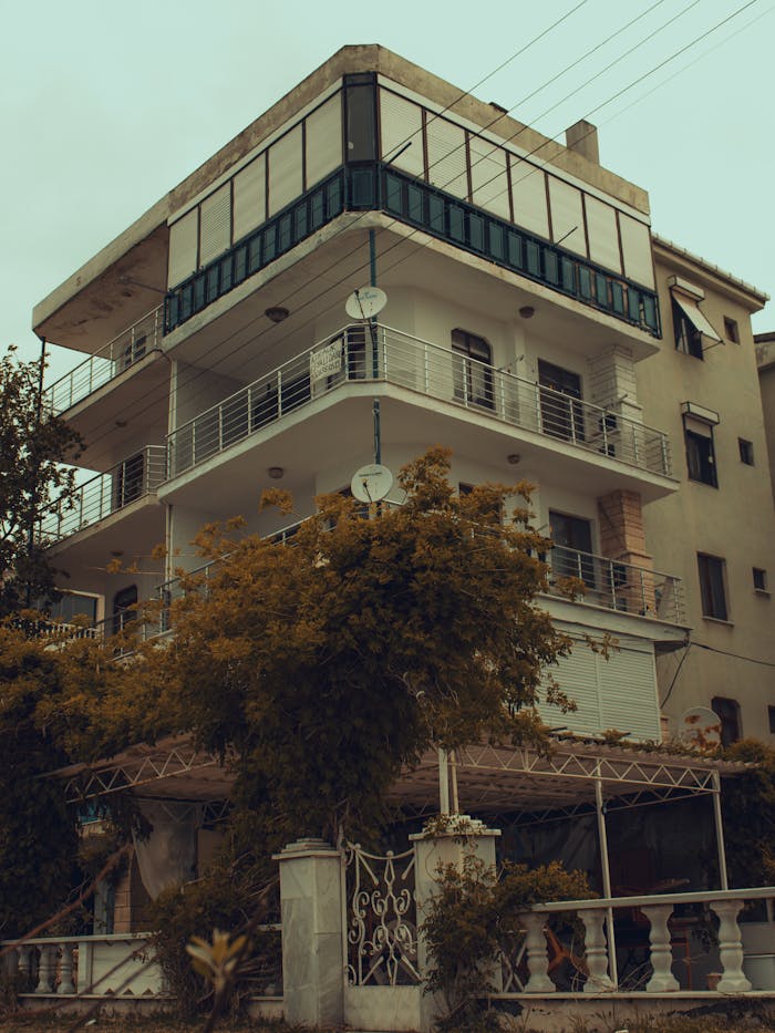 A tall urban residential building with autumn foliage in the foreground, shot during the day.