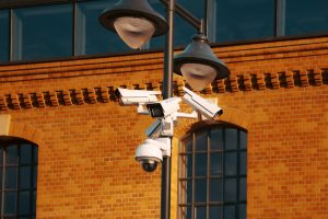 Modern security cameras mounted on a pole against a brick building in the city.