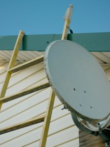 Close-up of a satellite dish and ladder on a house roof against a clear blue sky.