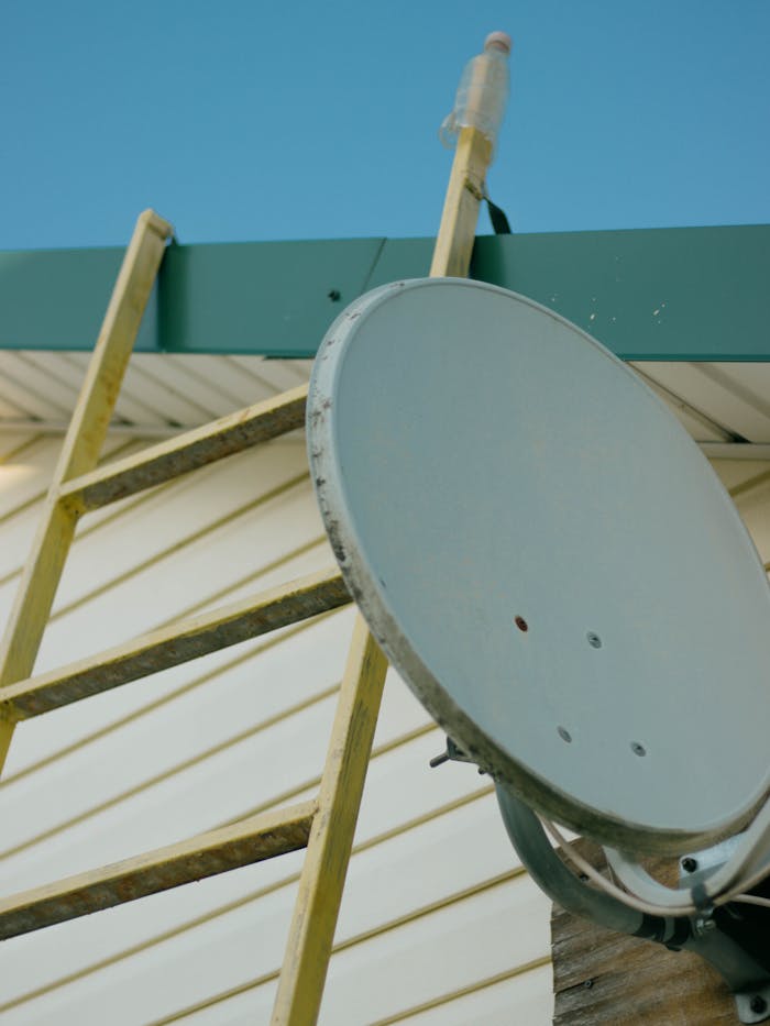 gallery-6 Close-up of a satellite dish and ladder on a house roof against a clear blue sky.